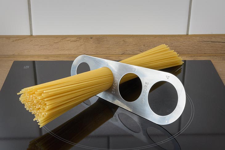 ein Nudel-Maß mit Spaghetti darin liegt auf einem Herd