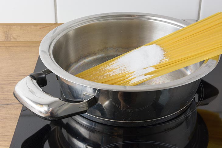 Spaghetti liegen in einem Topf mit viel Salz darauf